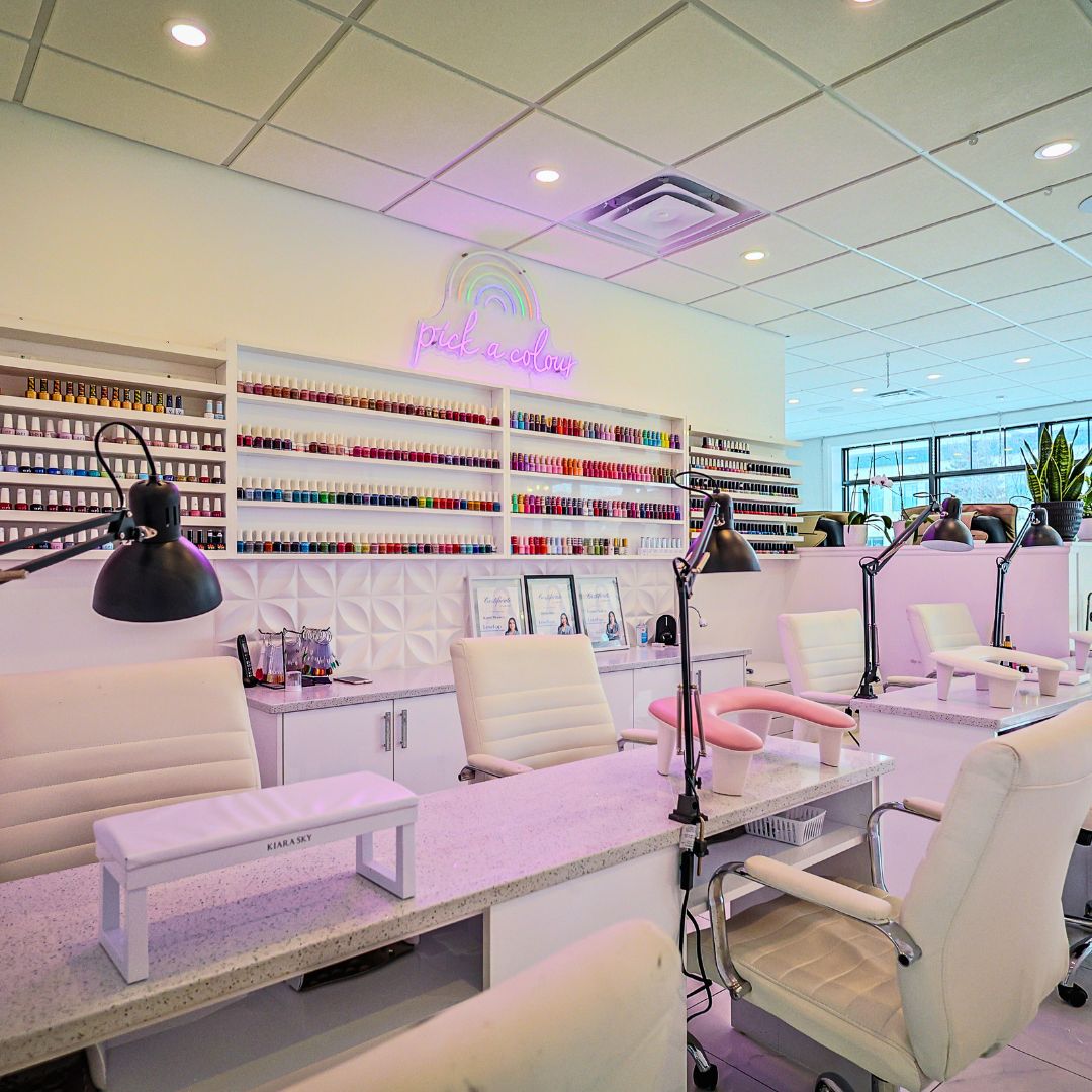 Nail salon interior with white chairs, tables, and shelves filled with nail polish.