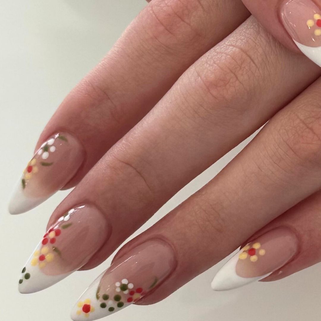 Almond-shaped nail enhancements with white French tips and colorful floral nail art, perfect for spring.