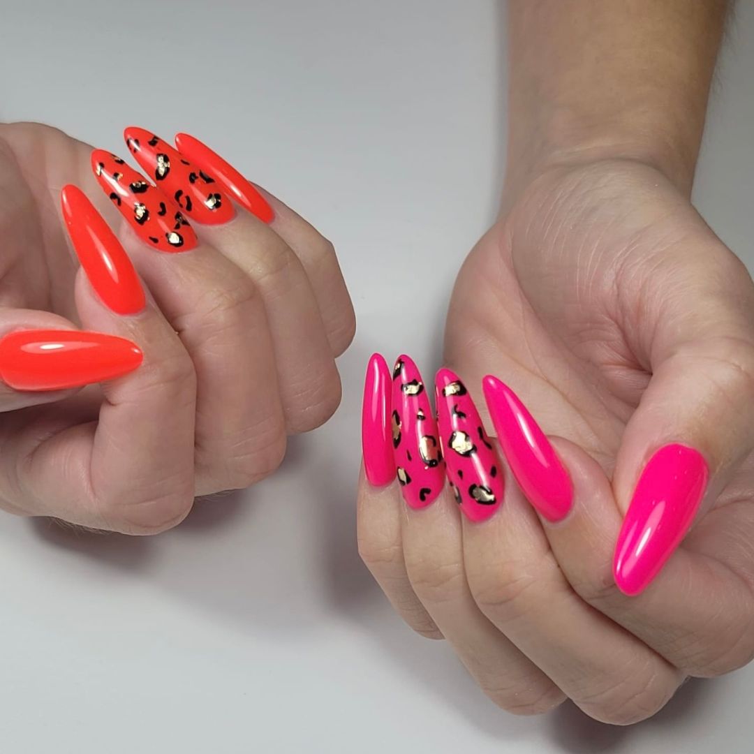 Long almond-shaped nail enhancements with neon pink and orange polish, featuring bold gold and black animal print nail art, created at our Grimsby salon.
