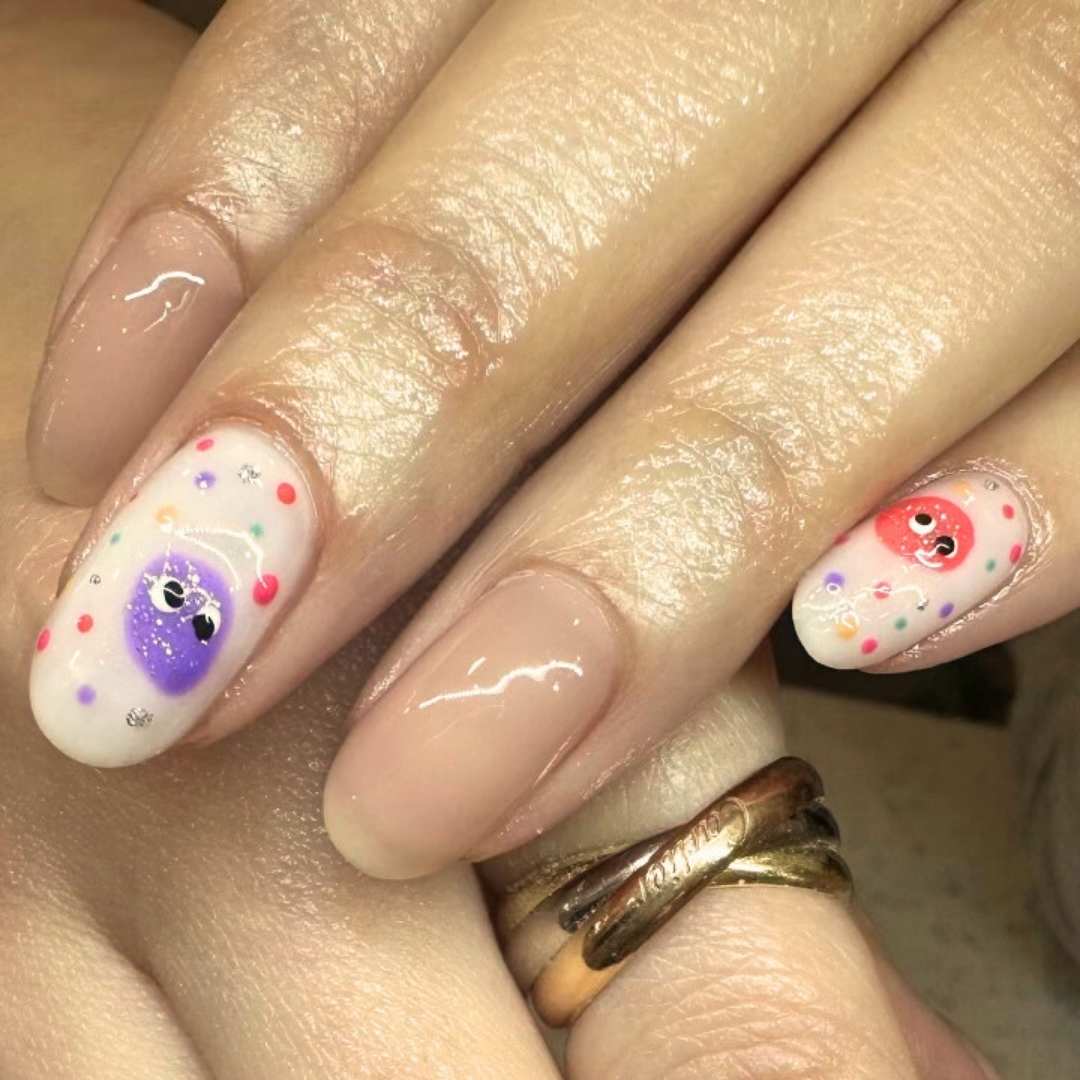 Playful manicure services showcasing glossy nude nails with hand-painted cute characters in purple and red, accented by colorful polka dots for a fun and whimsical look