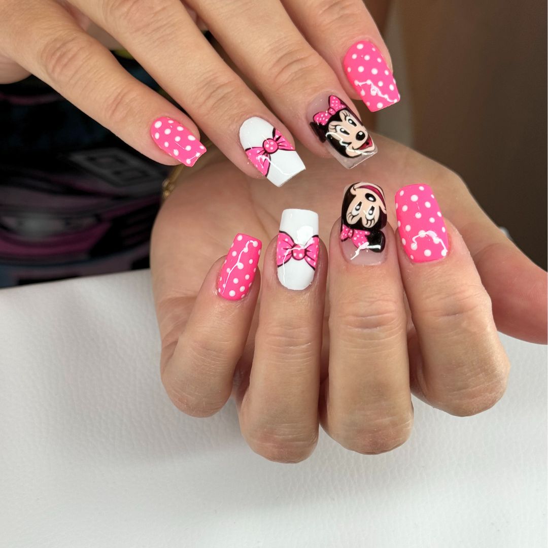 Custom nail art featuring Minnie Mouse faces, pink bows, and white polka dots on a pink and white base.
