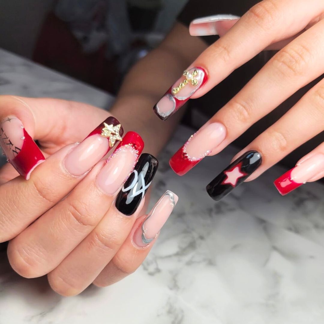 Coffin-shaped nail enhancements with red and black nail art, featuring 3D gold stars, abstract designs, and bold French tips.